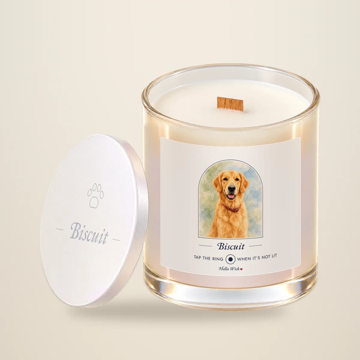 A Hello Wick candle labelled Biscuit, with a watercolour of the dog in an arch, its lid leaning beside it