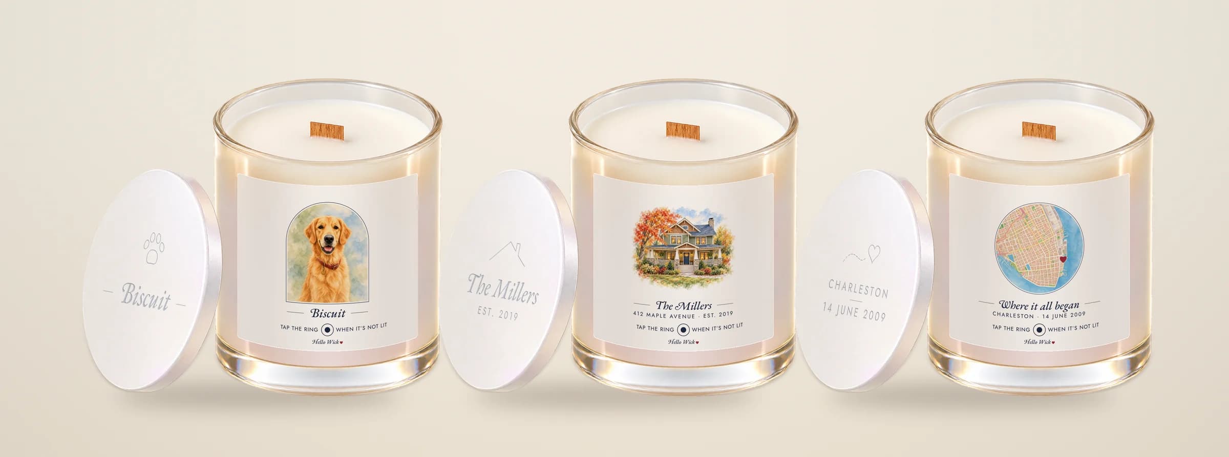 Three Hello Wick candles with their lids leaning beside them: Biscuit with a watercolour dog in an arch, The Millers with a watercolour house, and Where it all began with a round watercolour map of Charleston